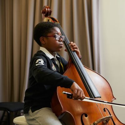 A boy with black hair and wearing a black long sleeved top plays the violin